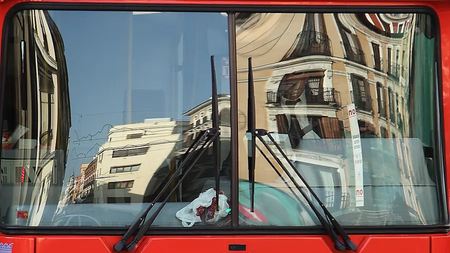Edificios de la calle Mayor reflejados en el parabrisas de un autobús rojo