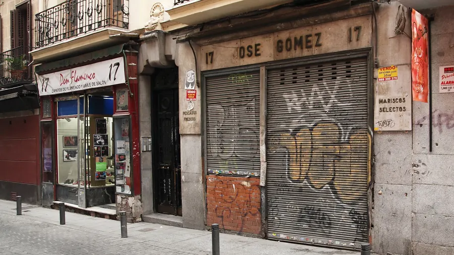 Fachada de una antigua pescadería cerrada, con persianas con grafitis, junto a una tienda de baile