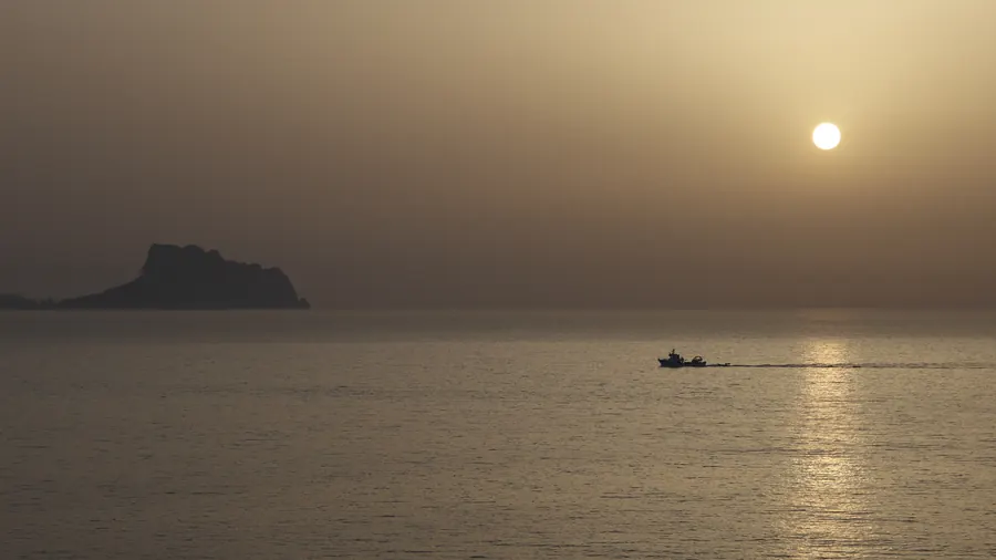 Un barco regresa a la costa al amanecer, con un peñón en el horizonte del Mediterráneo