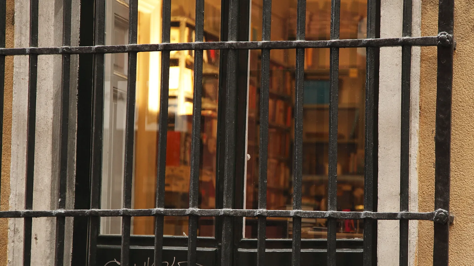 Ventana con reja de hierro tras la que se ve una biblioteca con estanterías llenas de libros
