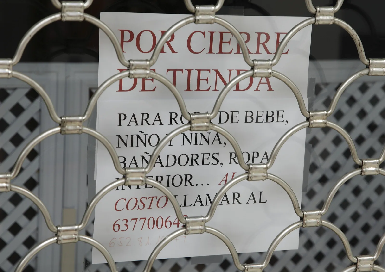 Cartel de cierre de una tienda de ropa colgado detrás de una reja metálica