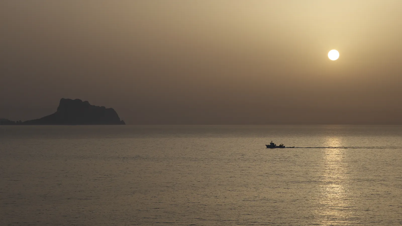 Un barco regresa a la costa al amanecer, con un peñón en el horizonte del Mediterráneo