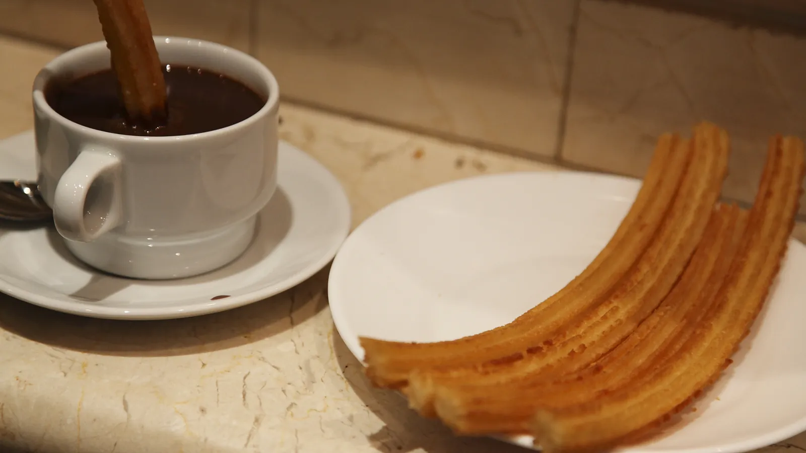 Una taza de chocolate caliente junto a un plato de churros